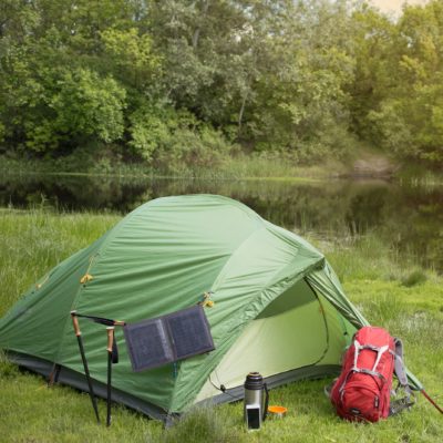 Image of tent set up in green grass, near water, with backpack in front.